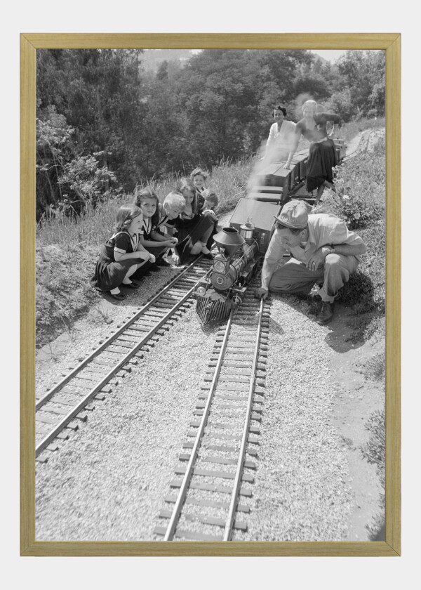 WALT DISNEY, SQUATTING NEXT TO HIS SCALE MODEL STEAM RAILROAD