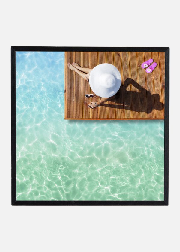 TANNING WOMAN WEARING SUN HAT AT THE POOL ON A WOODEN PIER SHOT FROM ABOVE