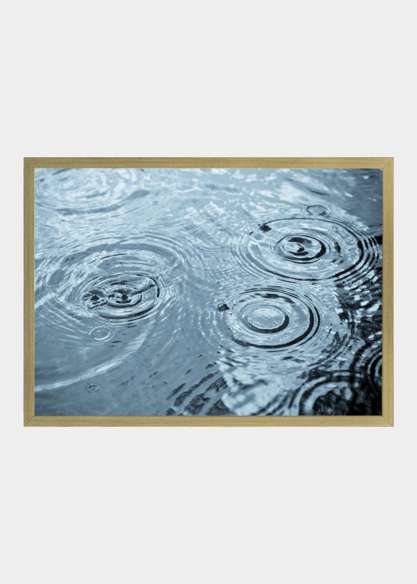 RAIN DROPS RIPPLING IN A PUDDLE WITH BLUE SKY REFLECTION